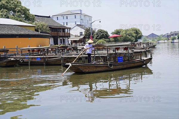 Excursion to Zhujiajiao water village, Shanghai, China, Asia, Wooden boat on canal with view of historical architecture, A calm river with a rowing boat and a rower in sunny weather, Asia