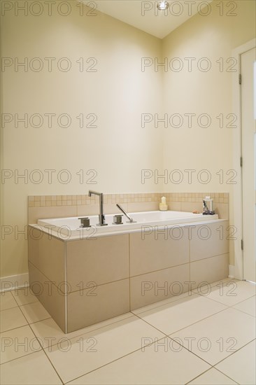 Soaking tub encased in a ceramic tile base in bathroom inside a renovated ground floor apartment in an old residential cottage style home, Quebec, Canada, North America