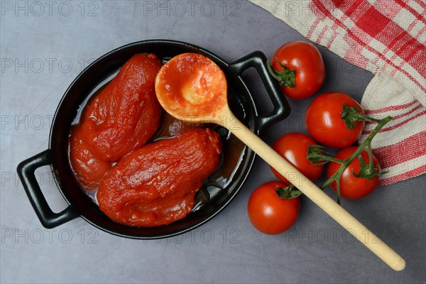 Whole tinned tomatoes in a pot, tomatoes and wooden spoon