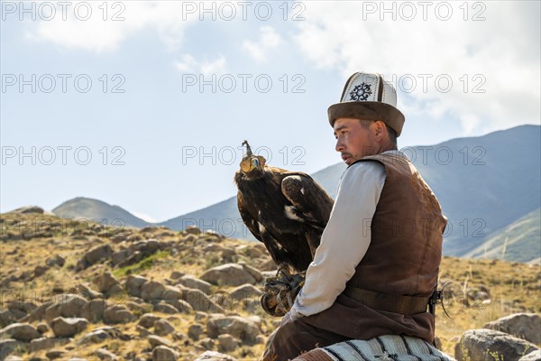 Traditional Kyrgyz eagle hunter riding with eagle in the mountains, hunting on horseback, near Bokonbayevo, Issyk Kul region, Kyrgyzstan, Asia