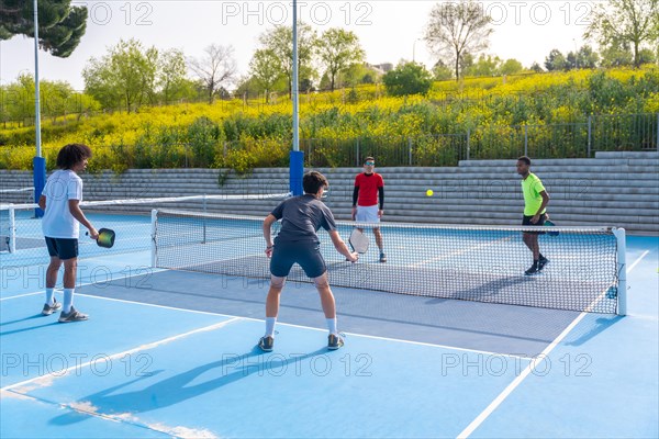 Full length photo of a group of four multi-ethnic friends playing pickleball in an outdoor court