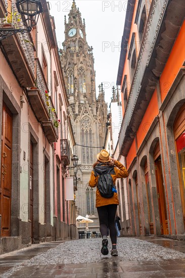 A tourist woman with a hat walking along a beautiful street next to the Church of San Juan Bautista, Arucas Cathedral, Gran Canaria, Spain, Europe