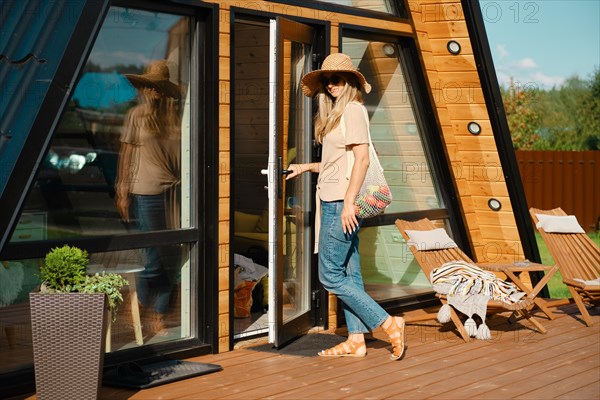 Mid-adult woman with string bag with vegetables on the porch of her log cabin