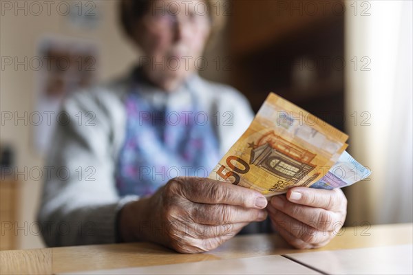 Senior citizen with wrinkled hands counts her money at home in her flat and holds banknotes in her hand, Cologne, North Rhine-Westphalia, Germany, Europe