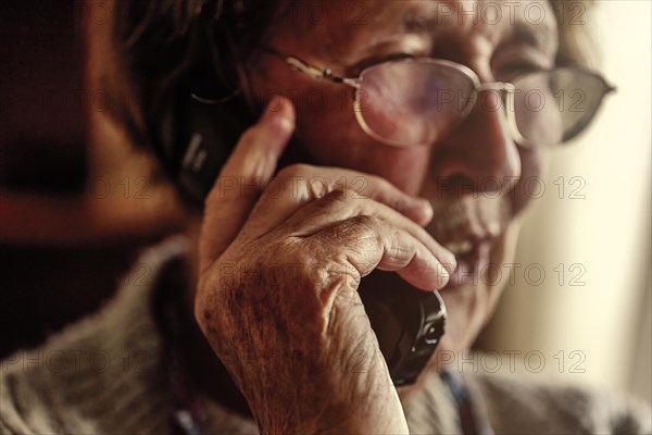 Senior citizen looks serious, frightened while talking on the phone in her living room, Cologne, North Rhine-Westphalia, Germany, Europe