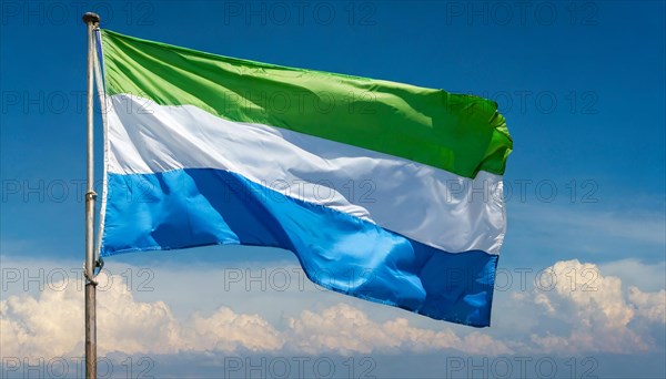 The flag of Sierra Leone, fluttering in the wind, isolated, against the blue sky