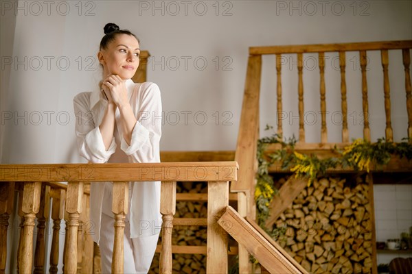 A woman looks thoughtfully into the distance while standing on a flight of stairs, resting her elbows on the railing