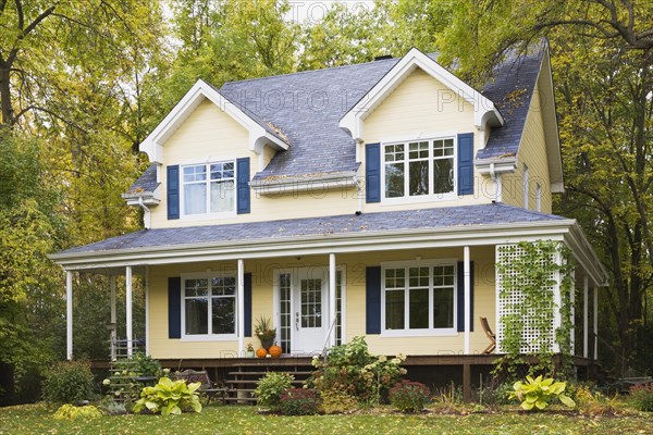 Two story yellow clapboard with blue and white trim cottage style home facade in autumn, Quebec, Canada, North America