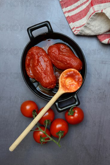 Whole tinned tomatoes in a pot, tomatoes and wooden spoon