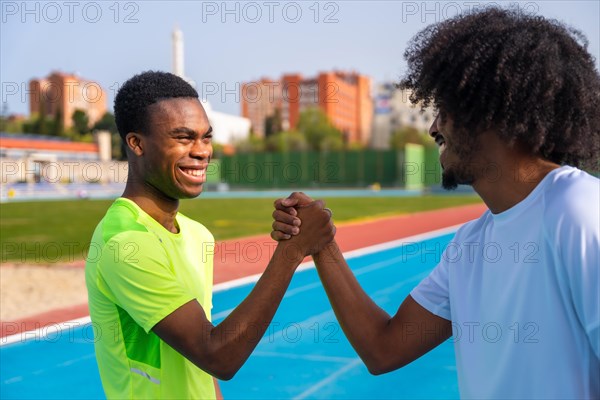 African american runner friends shaking hands while working out together in a running track