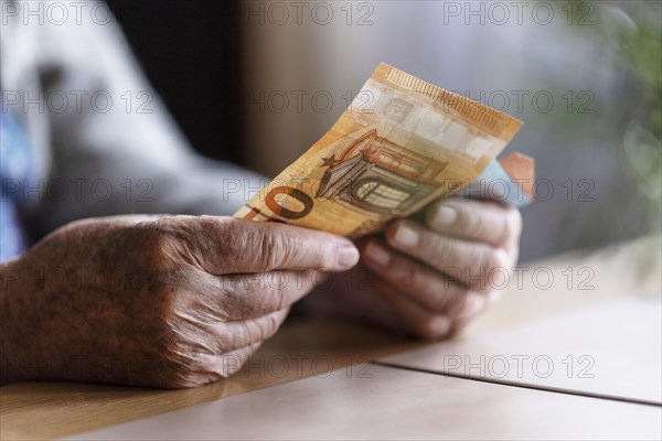 Senior citizen with wrinkled hands counts her money at home in her flat and holds banknotes in her hand, Cologne, North Rhine-Westphalia, Germany, Europe