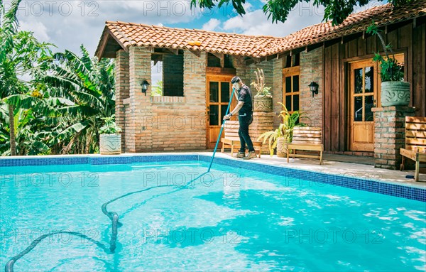 Maintenance and cleaning of home swimming pool with vacuum suction hose. Male worker cleaning a beautiful swimming pool with vacuum suction hose