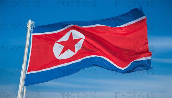The flag of North Korea flutters in the wind, isolated against a blue sky
