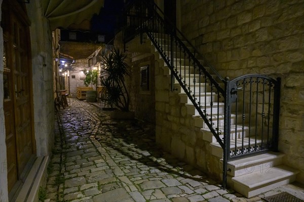A narrow alley illuminated at night with alleyway lamp and outdoor seating of a restaurant, Trogir, Dalmatia, Croatia, Europe
