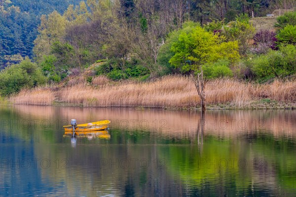 Small yellow metal fishing boat with small engine mount floating peacefully on a lake in South Korea