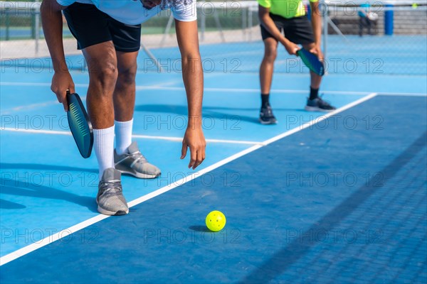 Cropped photo of the lower part of an african man bending to catch a pickleball ball from the floor in a court