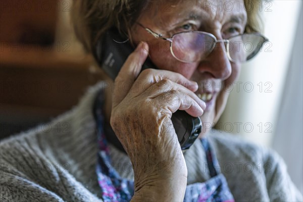 Senior citizen looks serious, frightened while talking on the phone in her living room, Cologne, North Rhine-Westphalia, Germany, Europe