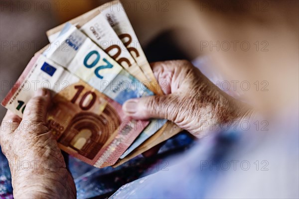 Senior citizen with wrinkled hands counts her money at home in her flat and holds banknotes in her hand, Cologne, North Rhine-Westphalia, Germany, Europe