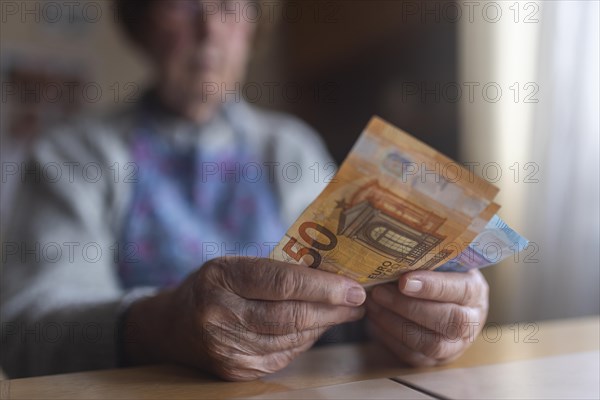 Senior citizen with wrinkled hands counts her money at home in her flat and holds banknotes in her hand, Cologne, North Rhine-Westphalia, Germany, Europe