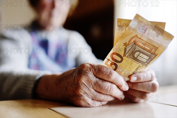 Senior citizen with wrinkled hands counts her money at home in her flat and holds banknotes in her hand, Cologne, North Rhine-Westphalia, Germany, Europe