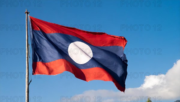 The flag of Laos flutters in the wind, isolated against a blue sky