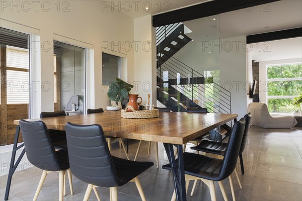 American walnut wood dining table and black leather sitting chairs with ash wood legs in dining room inside modern cube style home, Quebec, Canada, North America