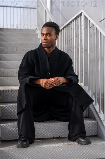 Vertical portrait of a stylish african handsome model sitting on stairs wearing winter black clothes