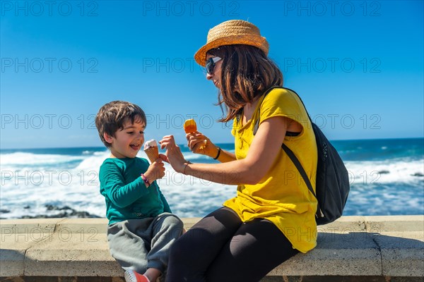 Mother with her little boy son eating ice cream by the sea on summer vacation