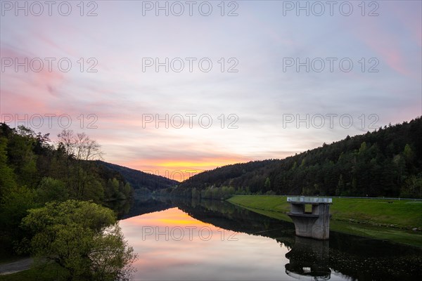 A lake in a landscape shot. A sunset and the natural surroundings are reflected in the water of the reservoir. Marbach reservoir, Odenwald, Hesse