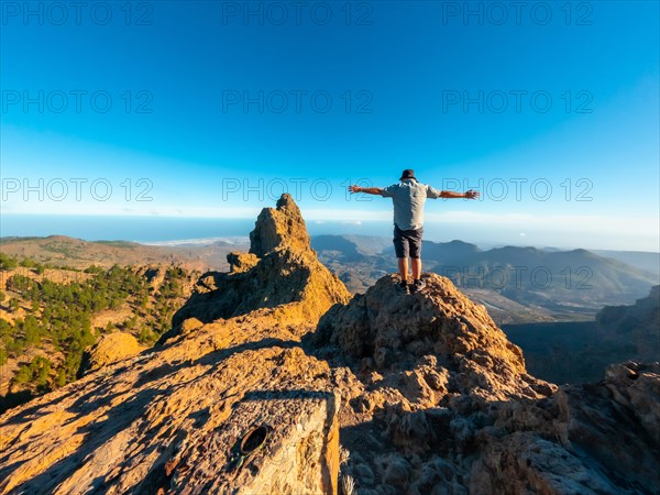 A tourist man with open arms on the top of Pico de las Nieves in Gran Canaria, Canary Islands