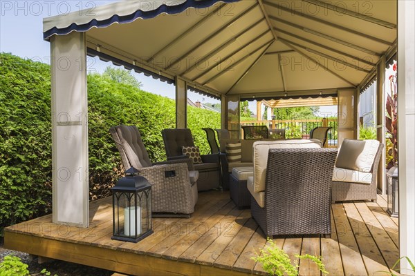 Gazebo on wooden deck furnished with wicker sitting chairs in backyard in summer, Quebec, Canada, North America