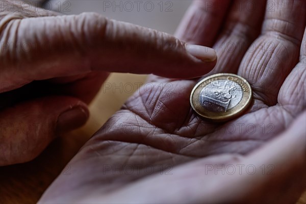 A euro coin in the wrinkled hand of a senior citizen, symbolising poverty and poverty in old age