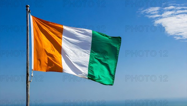 The flag of Ivory Coast flutters in the wind, isolated, against the blue sky