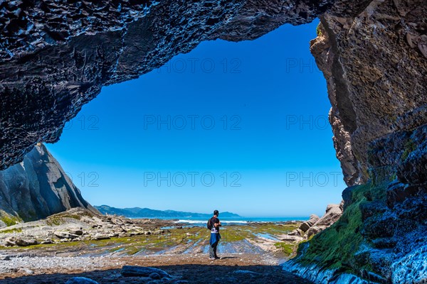 A hiker in the Algorri cove sea cave on the coast in the flysch of Zumaia, Gipuzkoa. Basque Country