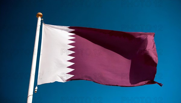 The flag of Qatar flutters in the wind, isolated against a blue sky