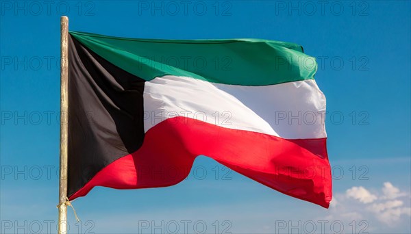 The flag of Kuwait flutters in the wind, isolated against a blue sky