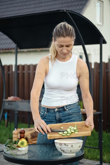 Woman adding sliced cucumber to a bowl with salad