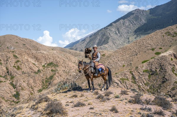 Traditional Kyrgyz eagle hunter riding with eagle in the mountains, hunting on horseback, near Bokonbayevo, Issyk Kul region, Kyrgyzstan, Asia