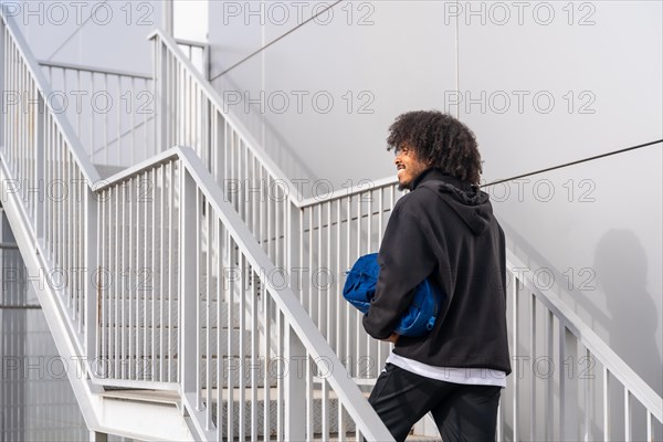 Rear view of an african sportive man carrying bag with pickleball racquet walking up stairs