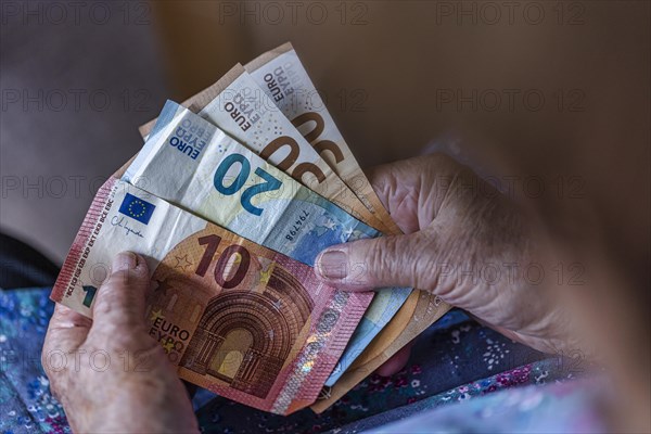 Senior citizen with wrinkled hands counts her money at home in her flat and holds banknotes in her hand, Cologne, North Rhine-Westphalia, Germany, Europe