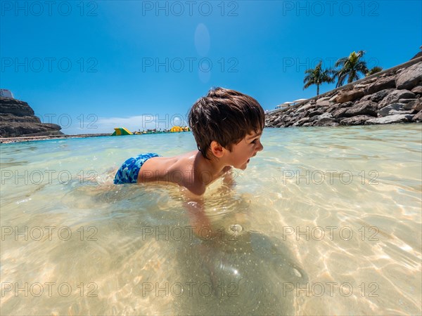 A young boy is swimming in the ocean. The water is clear and calm. The boy is wearing a blue swimsuit