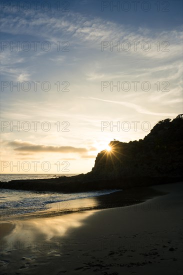 A beautiful sunset over the ocean with a bright sun shining on the water on a rocky beach