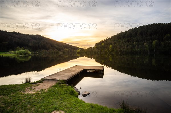 A lake in a landscape shot. A sunset and the natural surroundings are reflected in the water of the reservoir. Marbach reservoir, Odenwald, Hesse