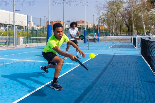 Man running to reach a ball playing pickleball with friend in an outdoor court