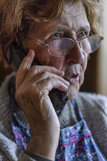 Senior citizen looks serious, frightened while talking on the phone in her living room, Cologne, North Rhine-Westphalia, Germany, Europe