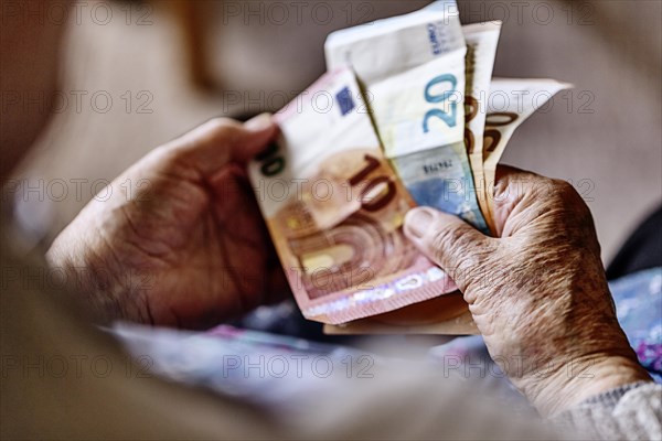 Senior citizen with wrinkled hands counts her money at home in her flat and holds banknotes in her hand, Cologne, North Rhine-Westphalia, Germany, Europe