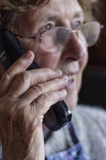 Senior citizen looks serious, frightened while talking on the phone in her living room, Cologne, North Rhine-Westphalia, Germany, Europe