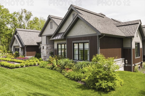 Contemporary natural stone and brown stained wood and cedar shingles clad luxurious bungalow style home facade in summer, Quebec, Canada, North America
