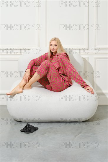 Barefoot woman in pink pyjama sitting on couch in a bright room