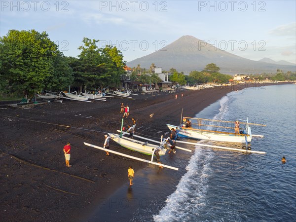 Fishermen loading fish from their outrigger boats in the morning on the black beach of Amed, Mount Agung in the background, Amed, Karangasem, Bali, Indonesia, Asia